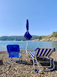 Deck chairs on beach against clear blue sky