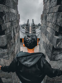 Rear view of man standing by building against sky