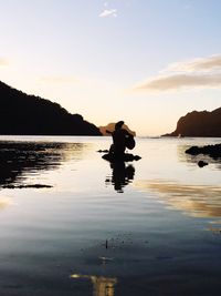 Silhouette man in sea against sky during sunset