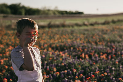 Boy holding flower against face while standing on field