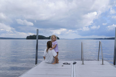 Rear view of women sitting on promenade by sea against sky
