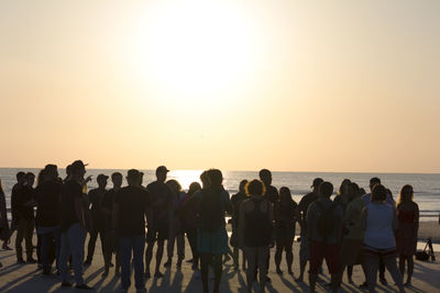 People standing on beach against clear sky during sunset