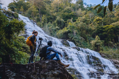 Friends photographing waterfall in forest