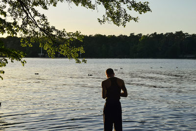 Rear view of man looking at lake against sky