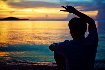Silhouette man gesturing peace sign at beach during sunset