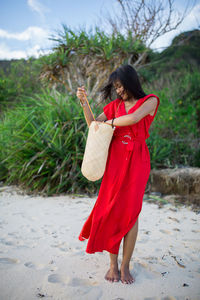 Young woman with shoulder bag standing on sandy beach