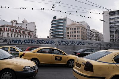 Vehicles on road by buildings in city against sky