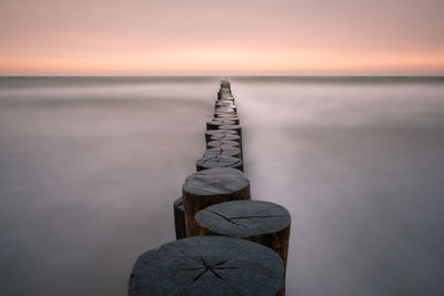 Groynes at beach in silent sea during sunset