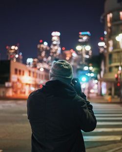 Rear view of man standing on city street at night