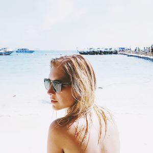 Portrait of young woman wearing sunglasses on beach against sky