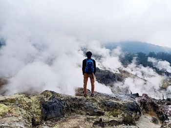 Rear view of man standing on rock against sky