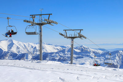 Cable car supports with chairs and skiers. against the background of snow ridges and blue sky