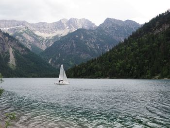 Sailboat sailing on sea against mountains