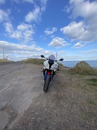 Rear view of man riding motorcycle on road against sky