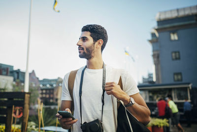 Tourist looking away while holding smart phone in city