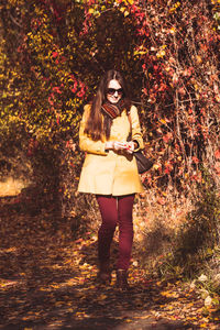 Full length portrait of young woman standing in park during autumn