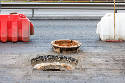 Red and white road shields protect an open sewer manhole during its repair on the carriageway.