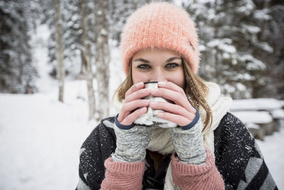 Portrait of young woman drinking hot drink outdoors in winter