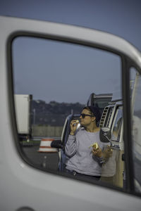 Woman eating banana reflecting on side-view mirror of car