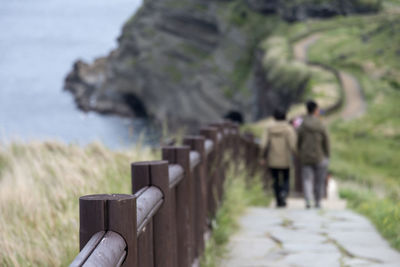 Rear view of friends walking on footpath by railing at beach