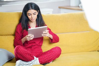 Woman using digital tablet while sitting on sofa