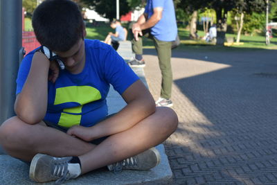 Rear view of boy sitting on footpath in city