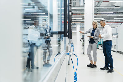 Businesswoman pointing at machinery and discussing with coworker in industry