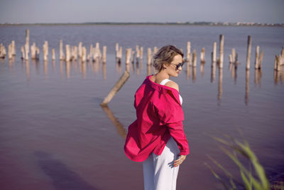 Portrait of young woman in pink and white clothes wearing sunglasses stand on pink lake 