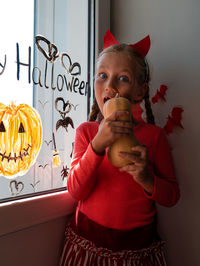 Child chewing pumpkin painting on window preparing to celebrate halloween little girl decorates room