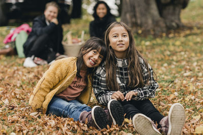 Happy friends sitting in park during autumn