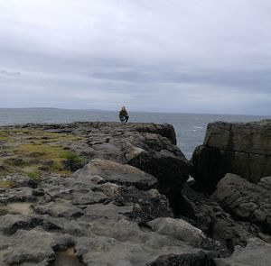 Young woman crouching on rocks against sea