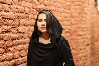 Beautiful young woman standing by brick wall