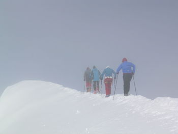 Rear view of friends walking on snowcapped mountain during winter