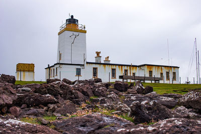 Lighthouse amidst rocks and buildings against sky