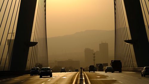 Cars on bridge in city against sky during sunset