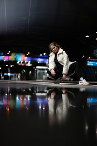 Reflection of woman crouching on reflective floor at night