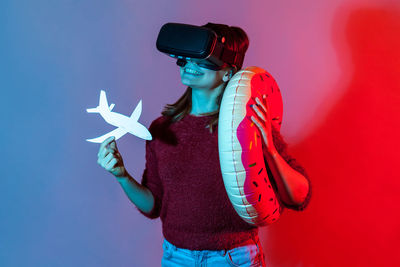 Woman wearing virtual reality simulator while standing against colored background