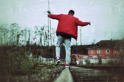 Rear view of man standing on wet railroad track during rainy day