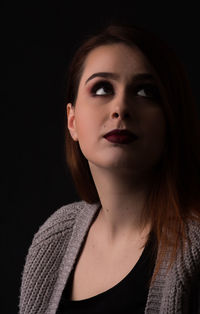 Close-up of woman wearing lipstick looking up against black background