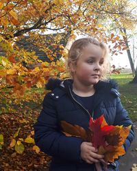 Girl looking away while holding autumn leaves in park