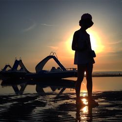 Silhouette of woman standing by sea at sunset