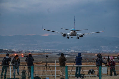 Rear view of people at airport runway against sky