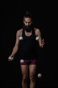 Bearded man playing with balls while standing against black background