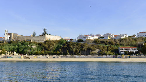 Scenic view of river by buildings against blue sky