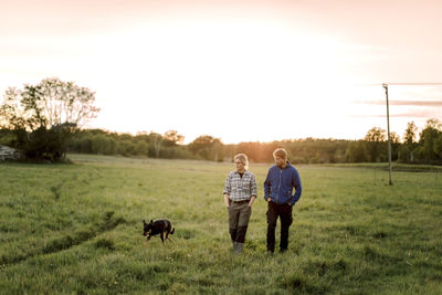 Mature couple with dog walking on field during sunset