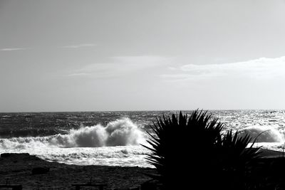 Waves crashing on rocks against sky