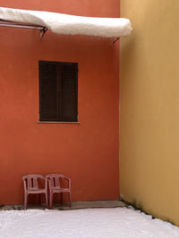 Empty chairs and tables against orange wall of building