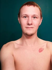 Portrait of handsome young man with lipstick kiss on chest against blue background