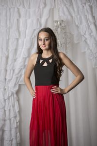 Portrait of young woman standing against curtain