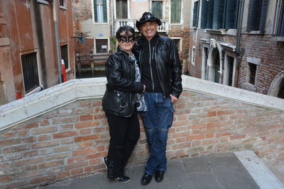 Full length portrait of young couple standing against brick wall